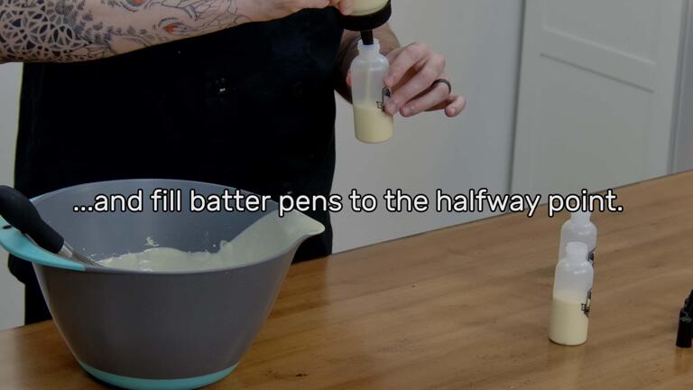 This image shows pancake batter being poured from a fill bottle into a batter pen, and says "...and fill batter pens to the halfway point."
