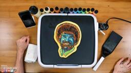 A pancake art portrait of Bob Ross with blue hues used for the face.